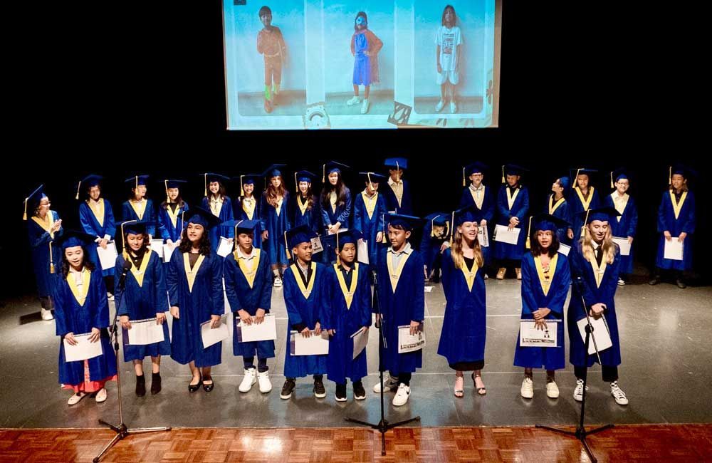 A group of graduates are standing on a stage singing into microphones.