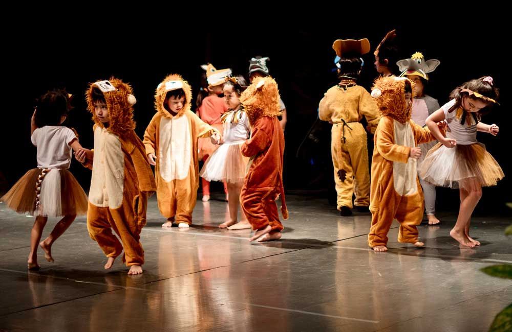 A group of children dressed in animal costumes are dancing on a stage.