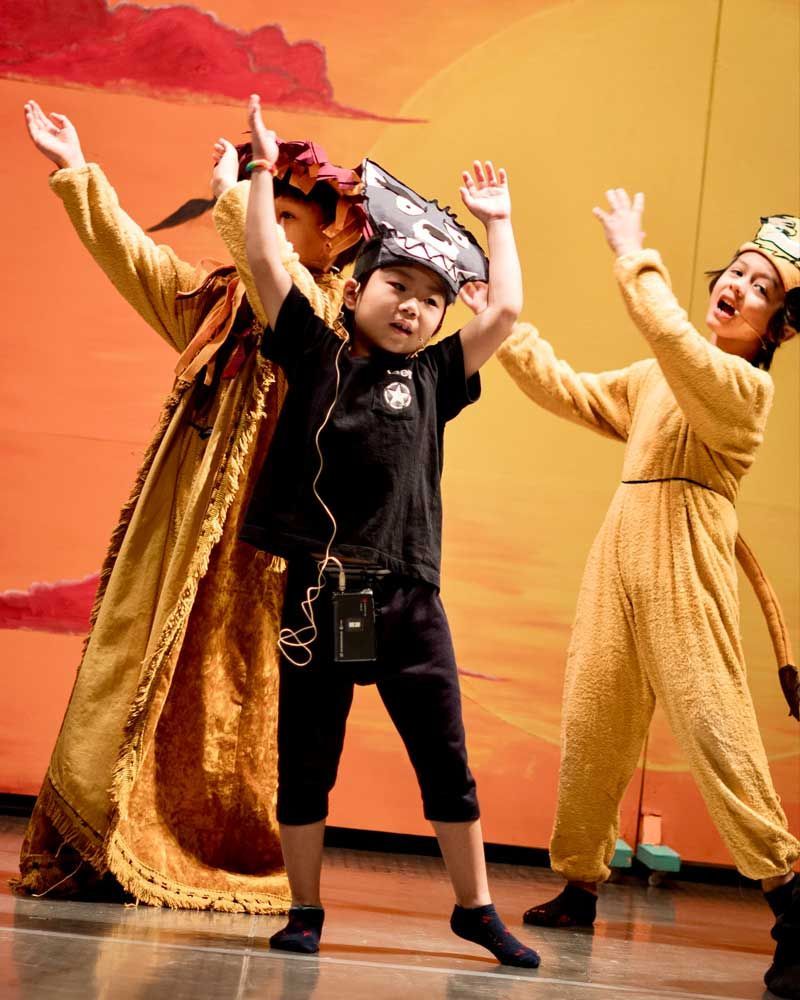 A group of children dressed in costumes are dancing on a stage