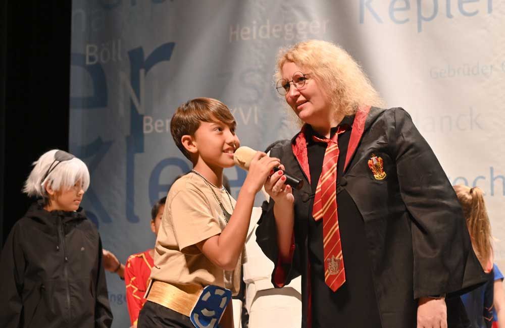 A woman in a harry potter costume is holding a microphone and talking to a young boy.