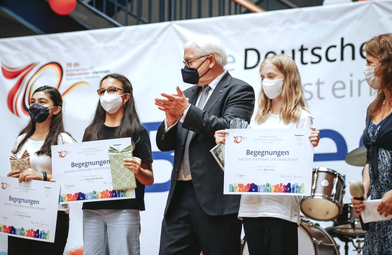 A group of people wearing face masks are standing in front of a sign that says deutsche