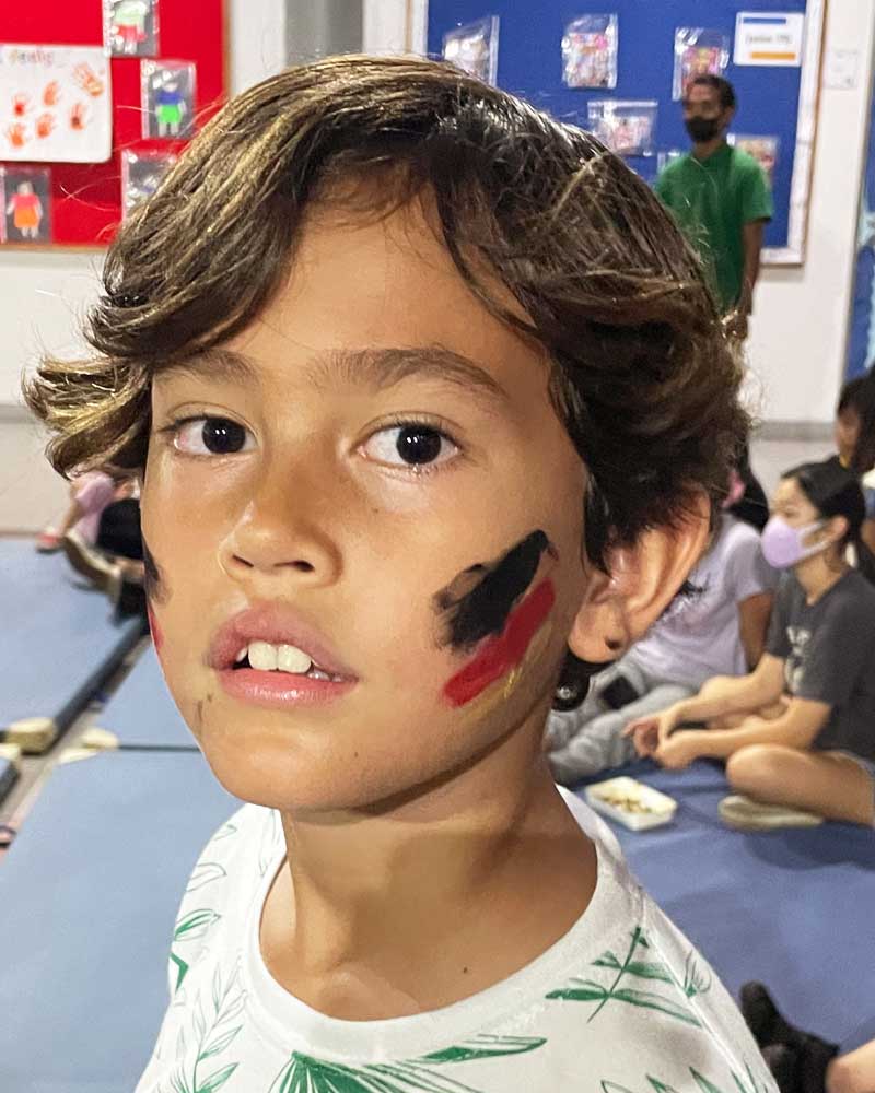 A young boy with paint on his face is sitting on the floor.