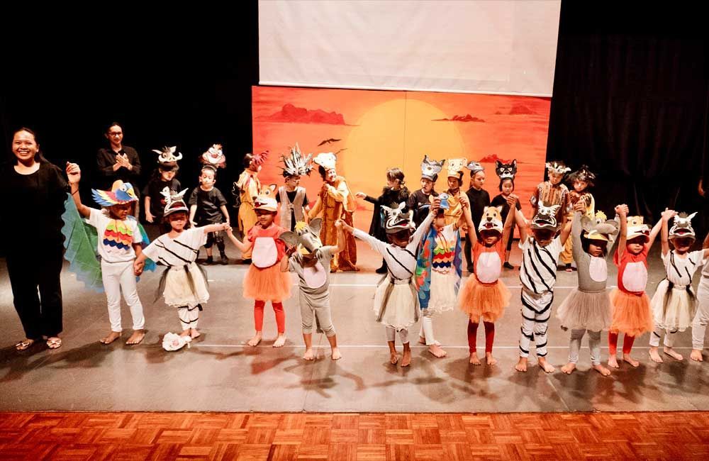 A group of children are standing on a stage holding hands.