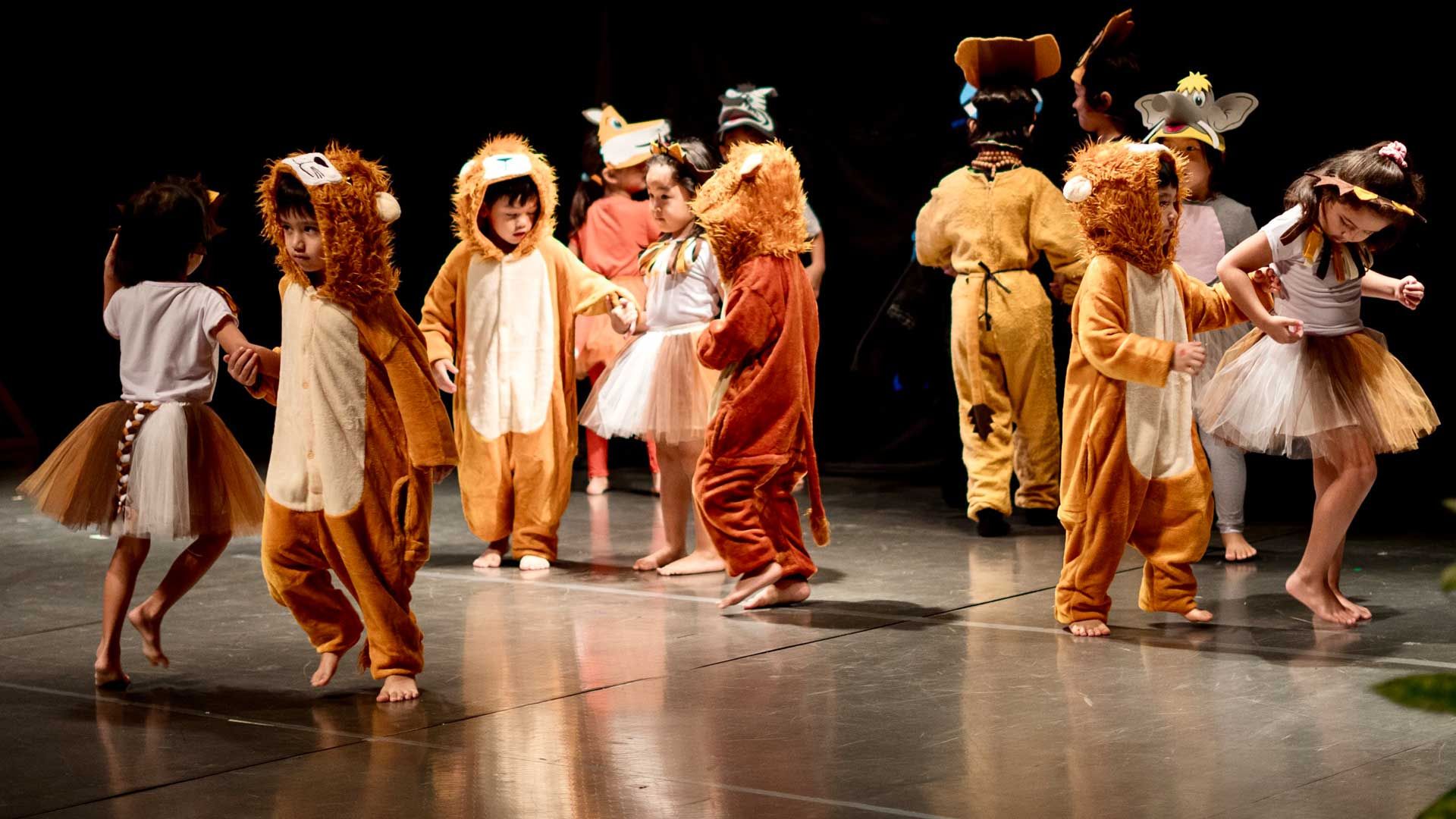 A group of children dressed in lion costumes are dancing on a stage.