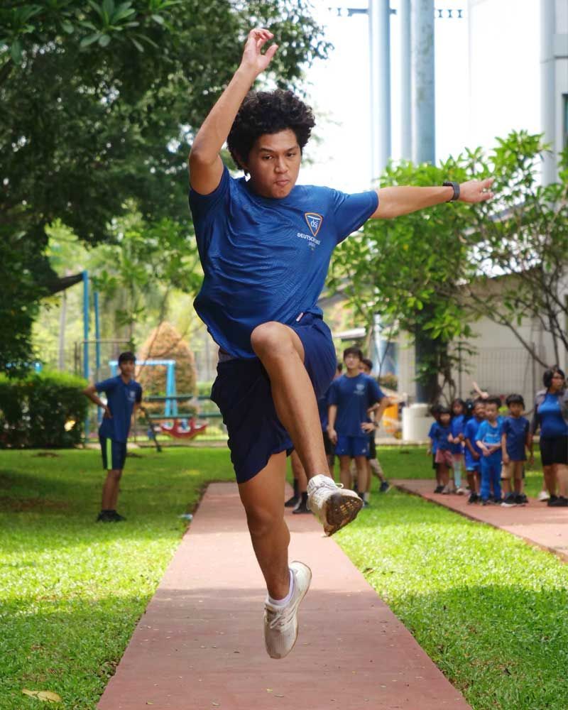 A young man in a blue shirt is jumping in the air.