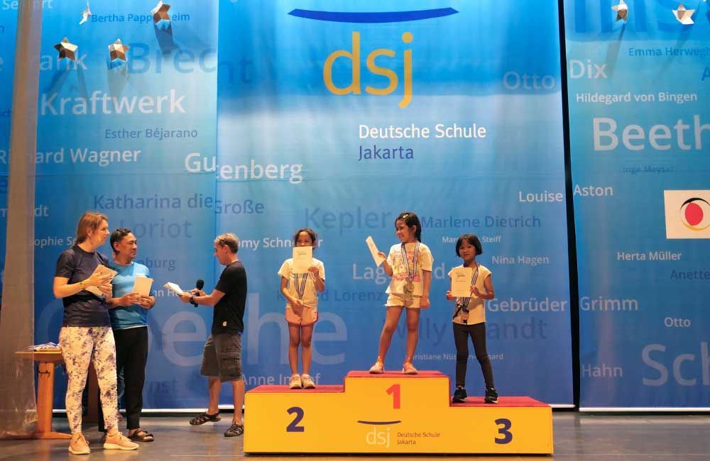 A group of children standing on a podium with the word dsj on the wall behind them