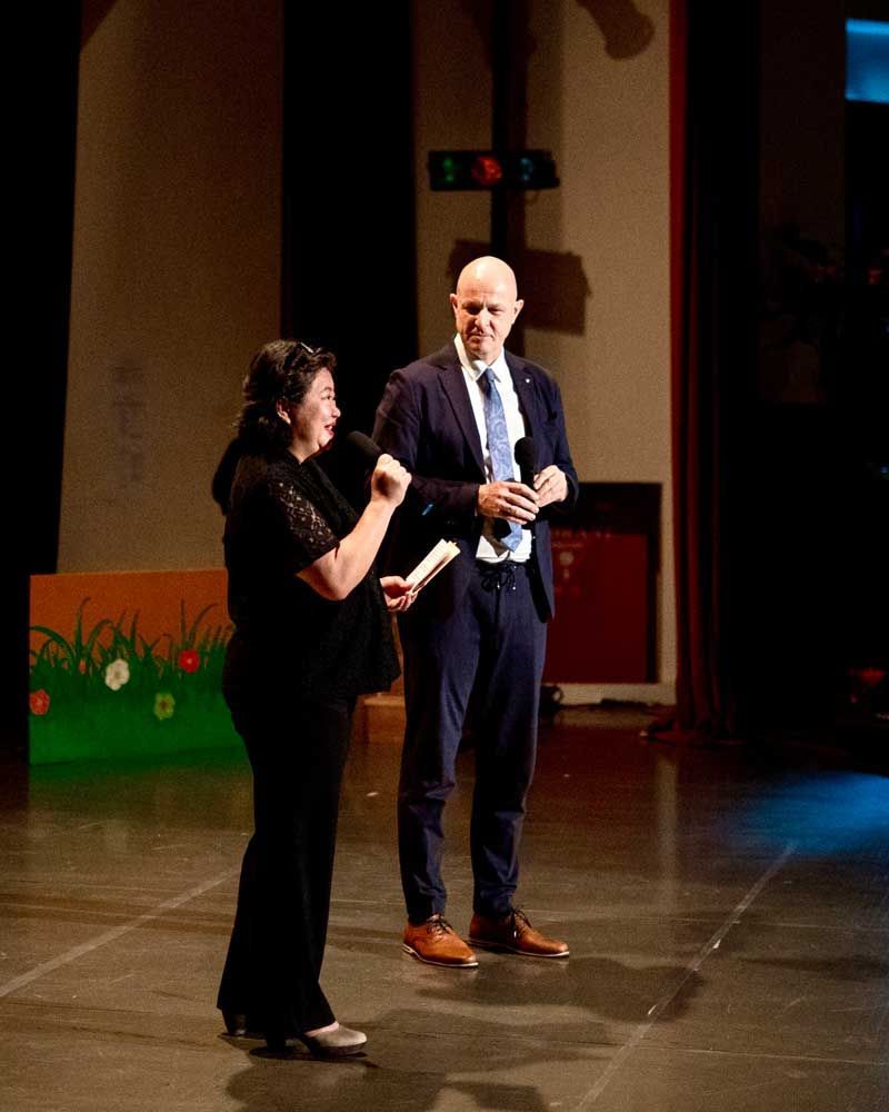 A man in a suit and tie stands next to a woman on a stage