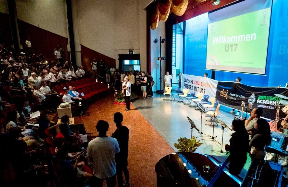 A large group of people are sitting in a large auditorium watching a presentation.