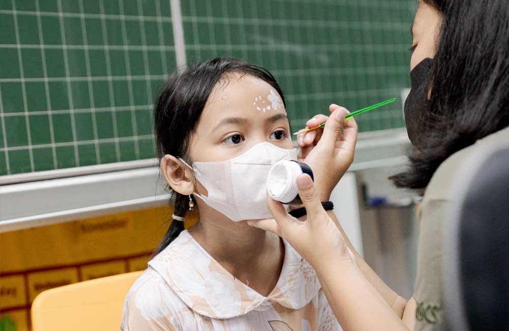 A woman is applying makeup to a little girl 's face.