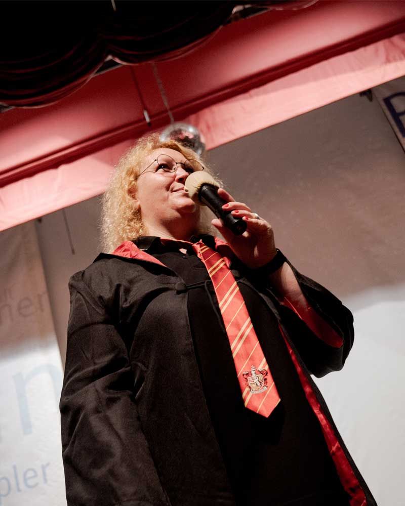A woman in a black gown and red tie is singing into a microphone
