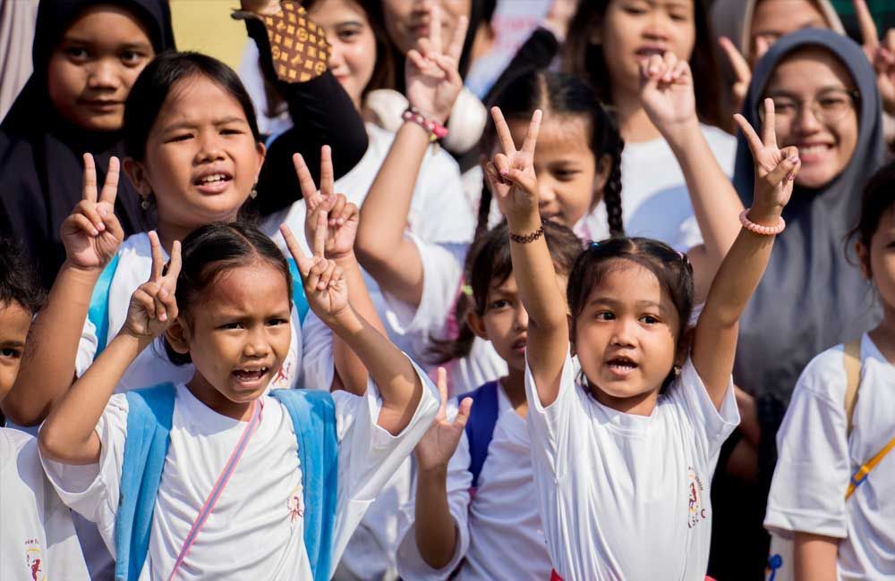 A group of children are giving peace signs with their hands in the air.