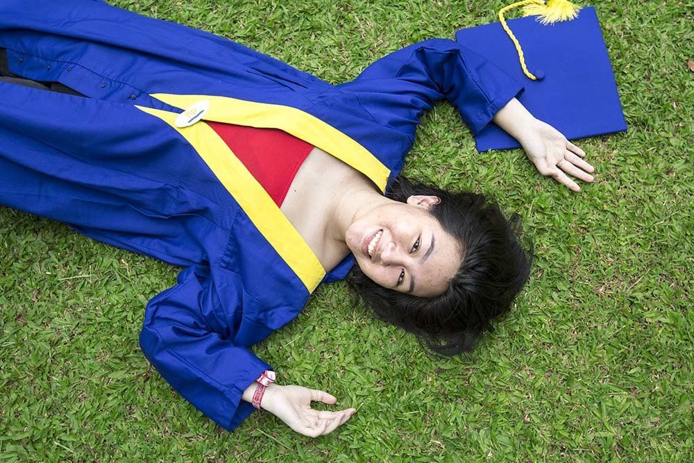 A woman in a graduation cap and gown is laying on the grass.