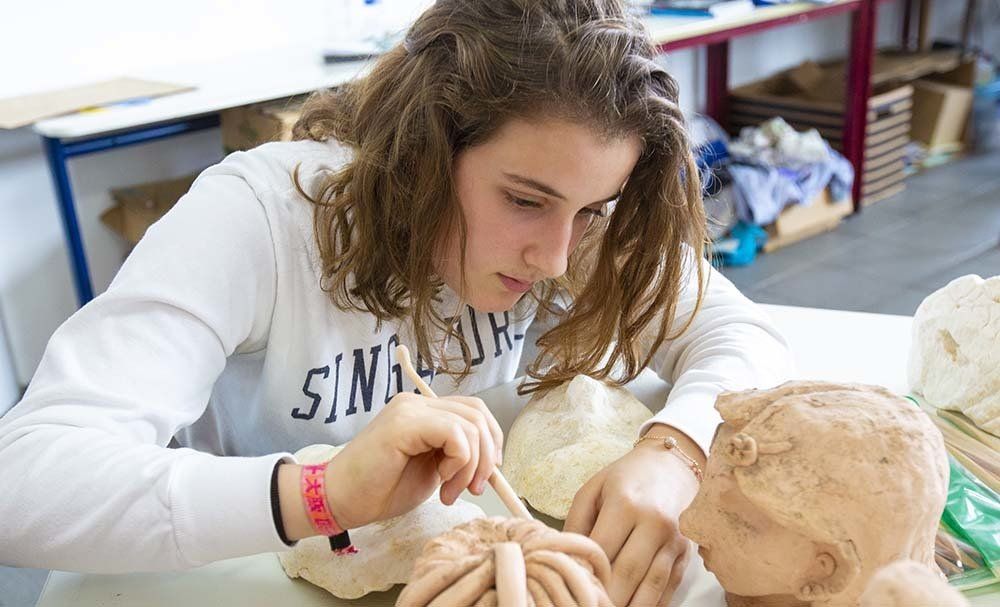 A young woman is sitting at a table working on a sculpture.