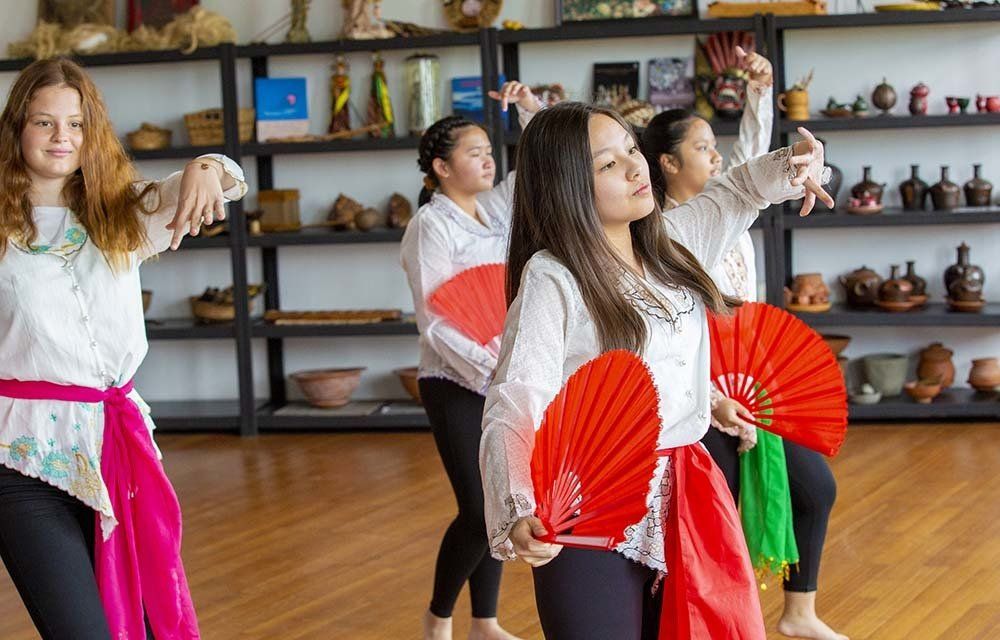 A group of young women are dancing with red fans in a room.