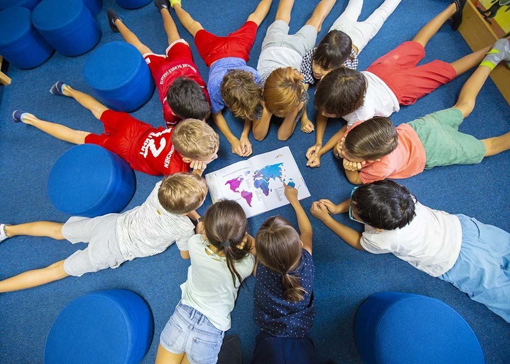A group of children are laying on the floor in a circle looking at a map of the world.