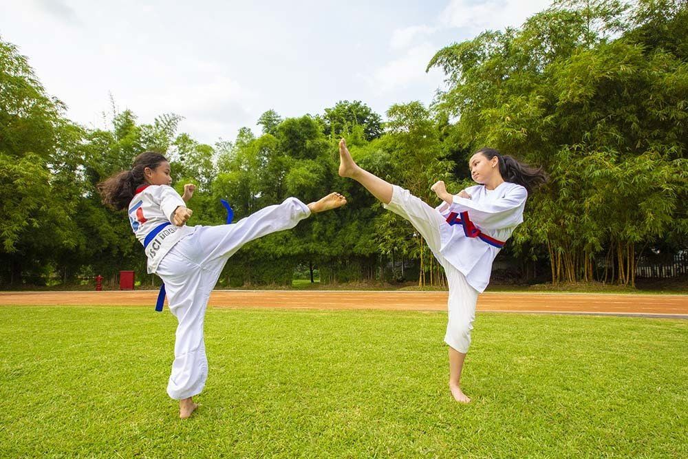 Two young women are practicing karate on a lush green field.