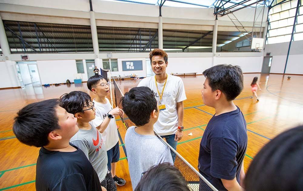 A man is talking to a group of young boys in a gym.