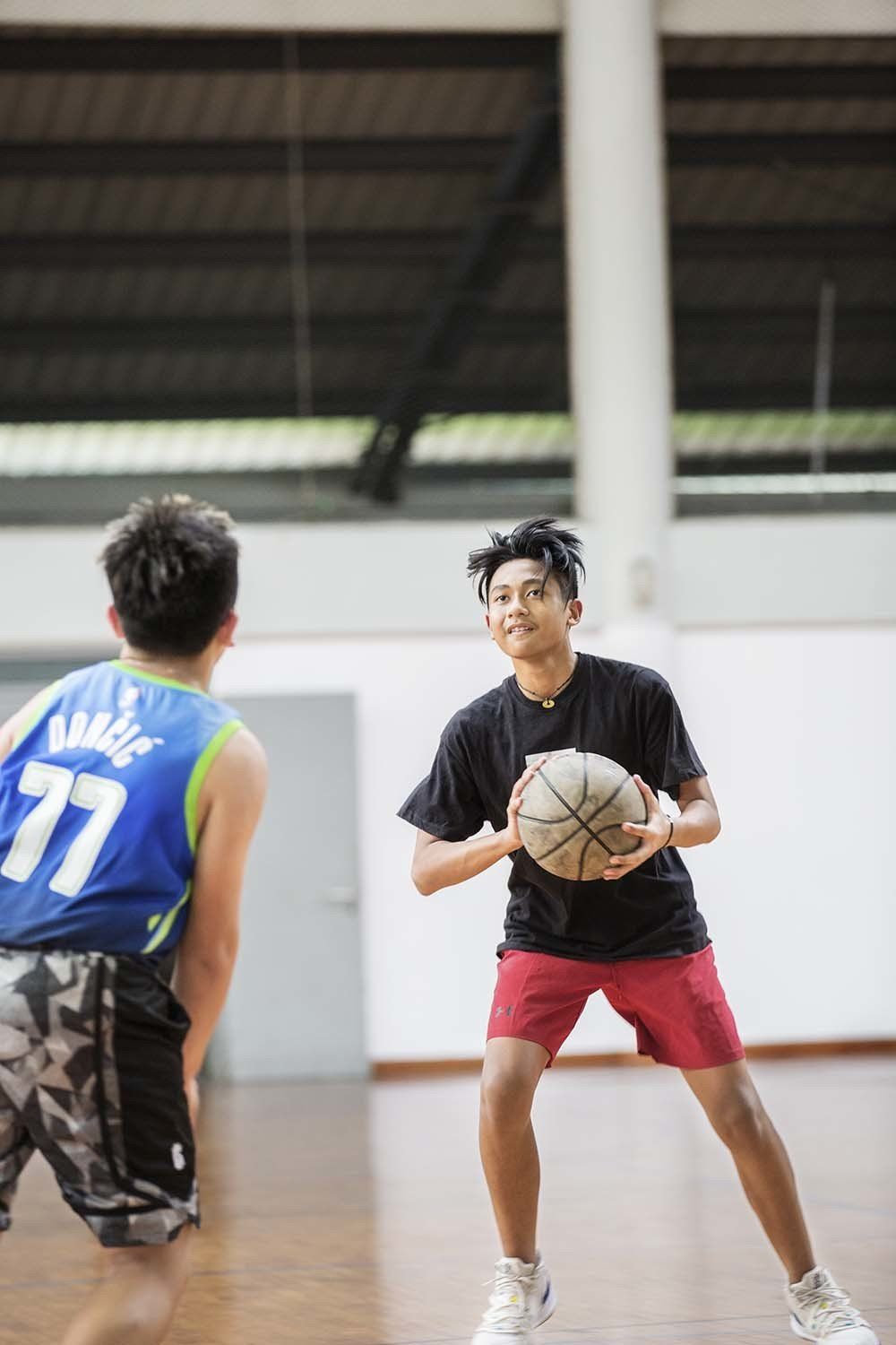 Two young men are playing basketball in a gym.