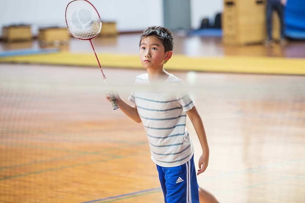 A young boy is playing badminton in a gym.