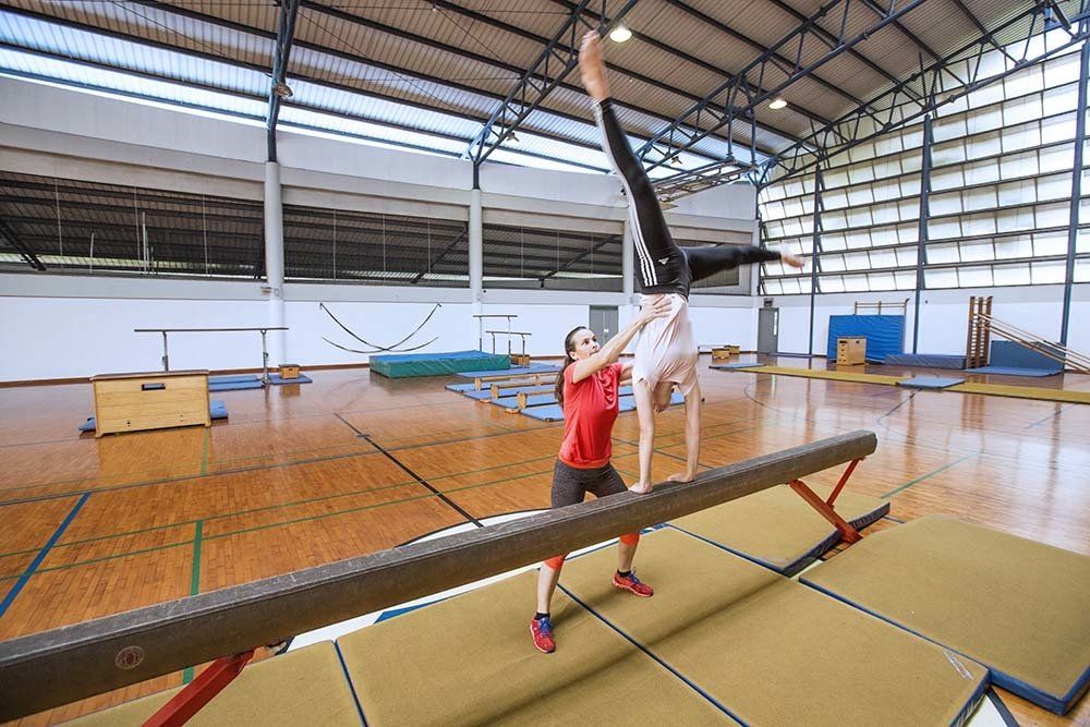 Two gymnasts are doing a handstand on a balance beam in a gym.