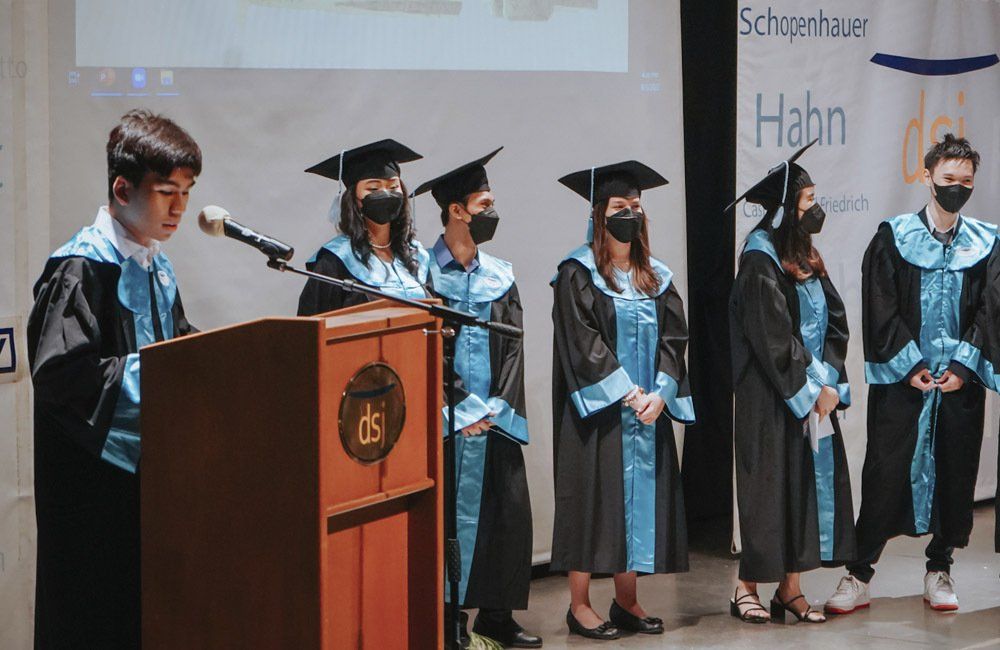 A group of graduates wearing masks are standing in front of a podium.