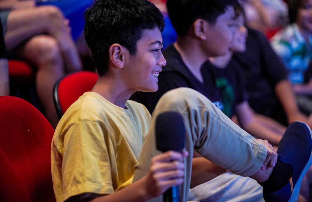 A young boy is sitting in a theater holding a microphone.