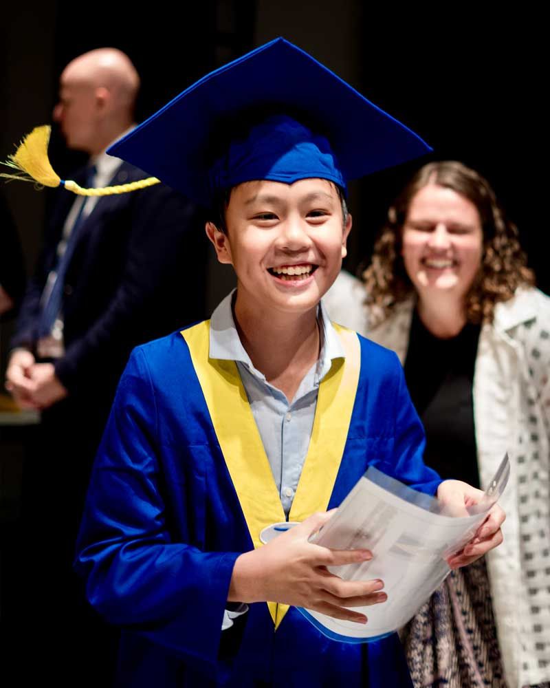 A young boy in a graduation cap and gown is holding a piece of paper.