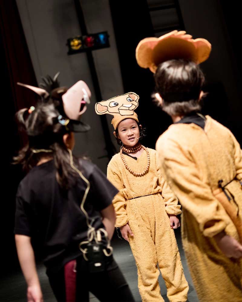 A group of children dressed in animal costumes are standing on a stage