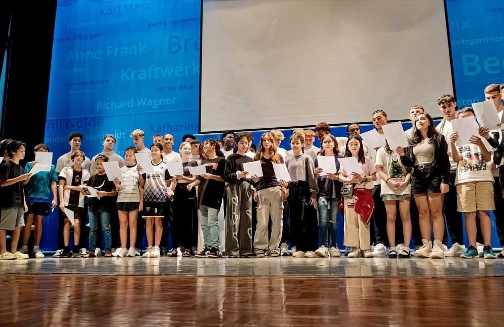 A large group of people are standing on a stage holding papers.