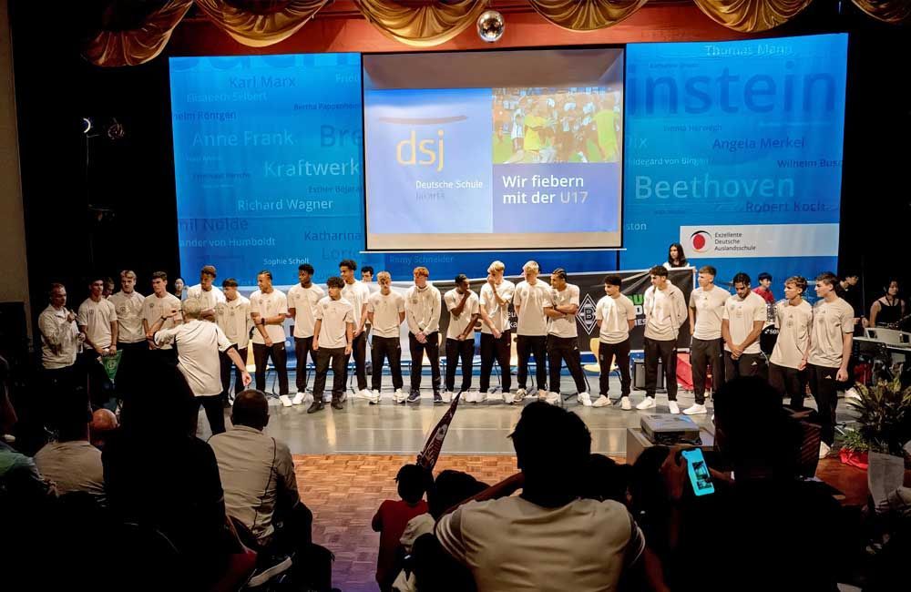 A group of people are standing on a stage in front of a large screen.