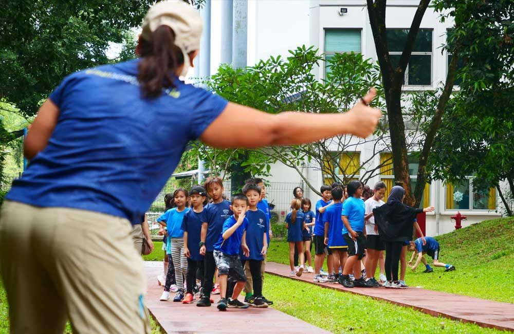 A woman in a blue shirt is standing in front of a group of children