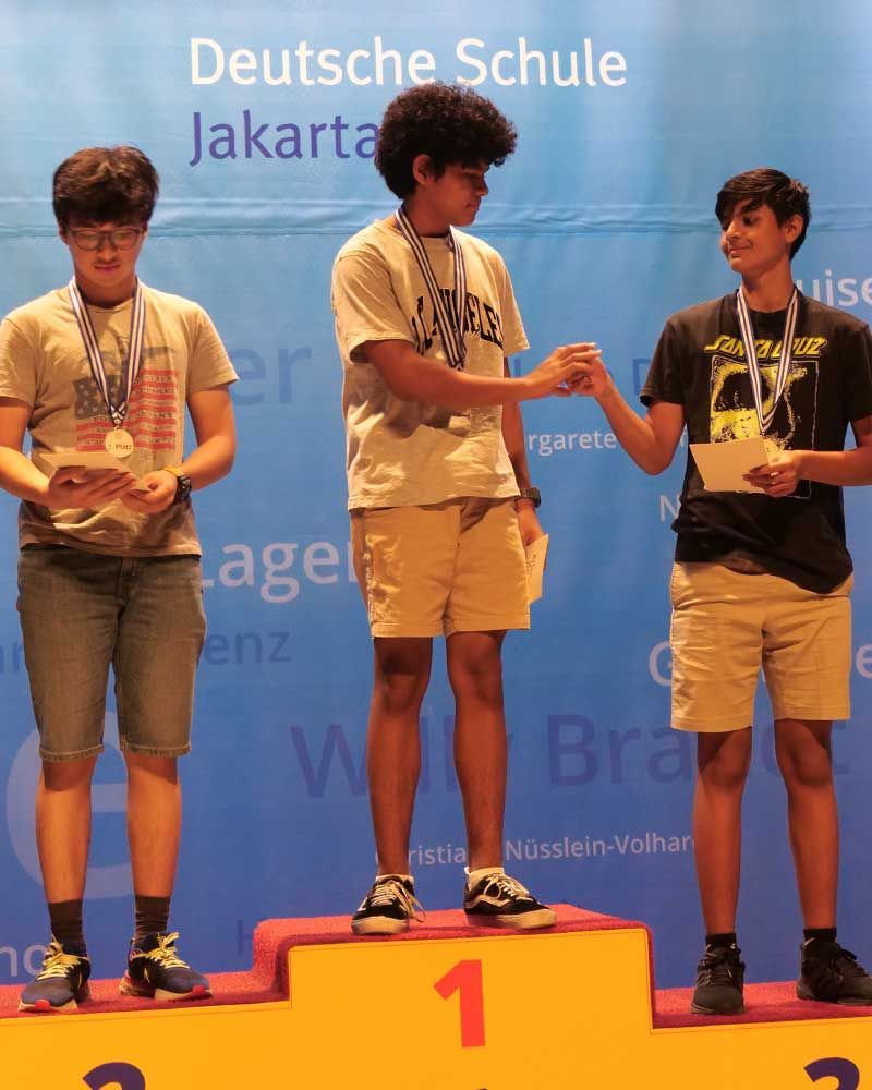 Three young men standing on a podium with the number 1 on it