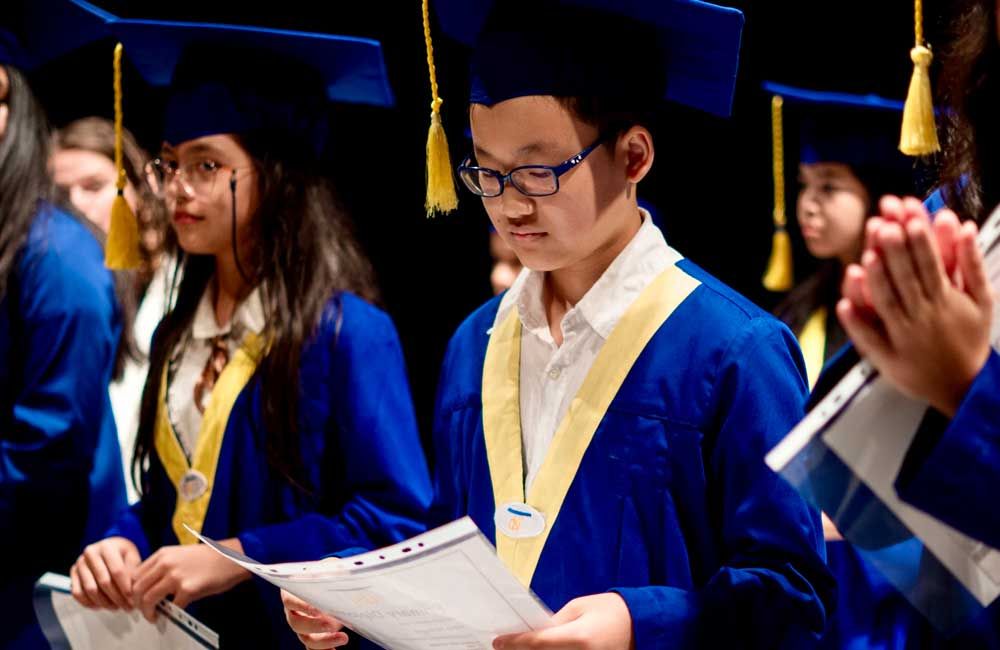 A boy in a graduation cap and gown is holding a piece of paper.