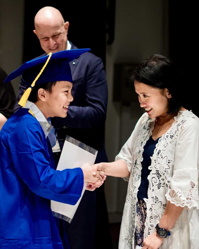 A boy in a graduation cap and gown shakes hands with a woman