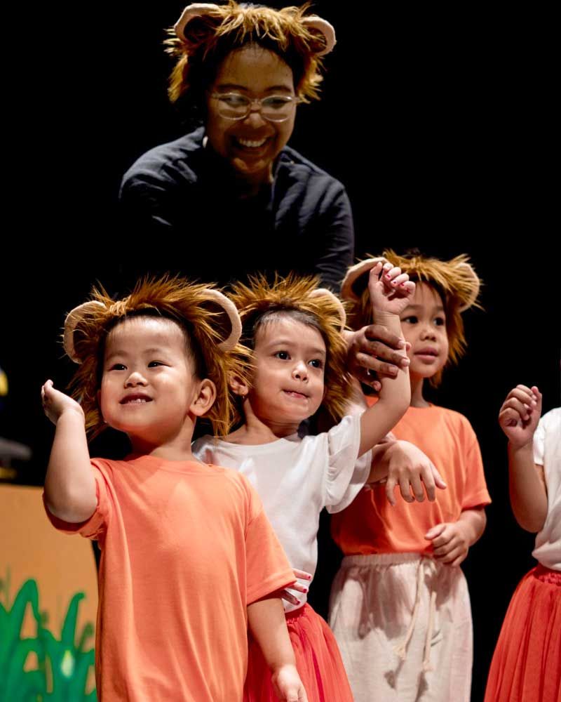 A group of children dressed in lion costumes are dancing on a stage.