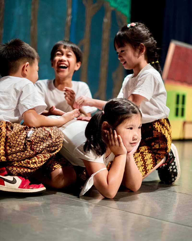 A group of children are sitting on the floor on a stage.