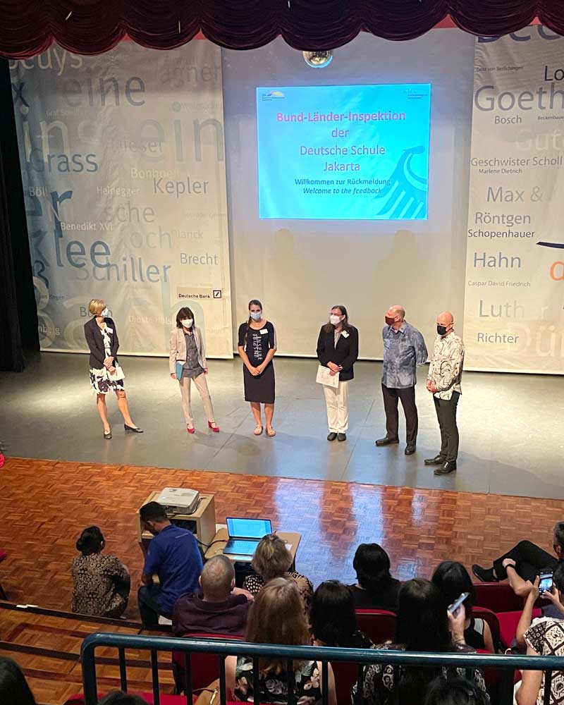 A group of people are standing on a stage in front of a large screen.