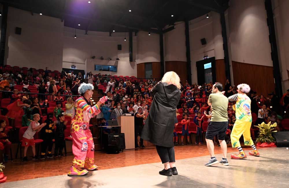 A lively performance on stage with clowns and other participants engaging with an enthusiastic audience