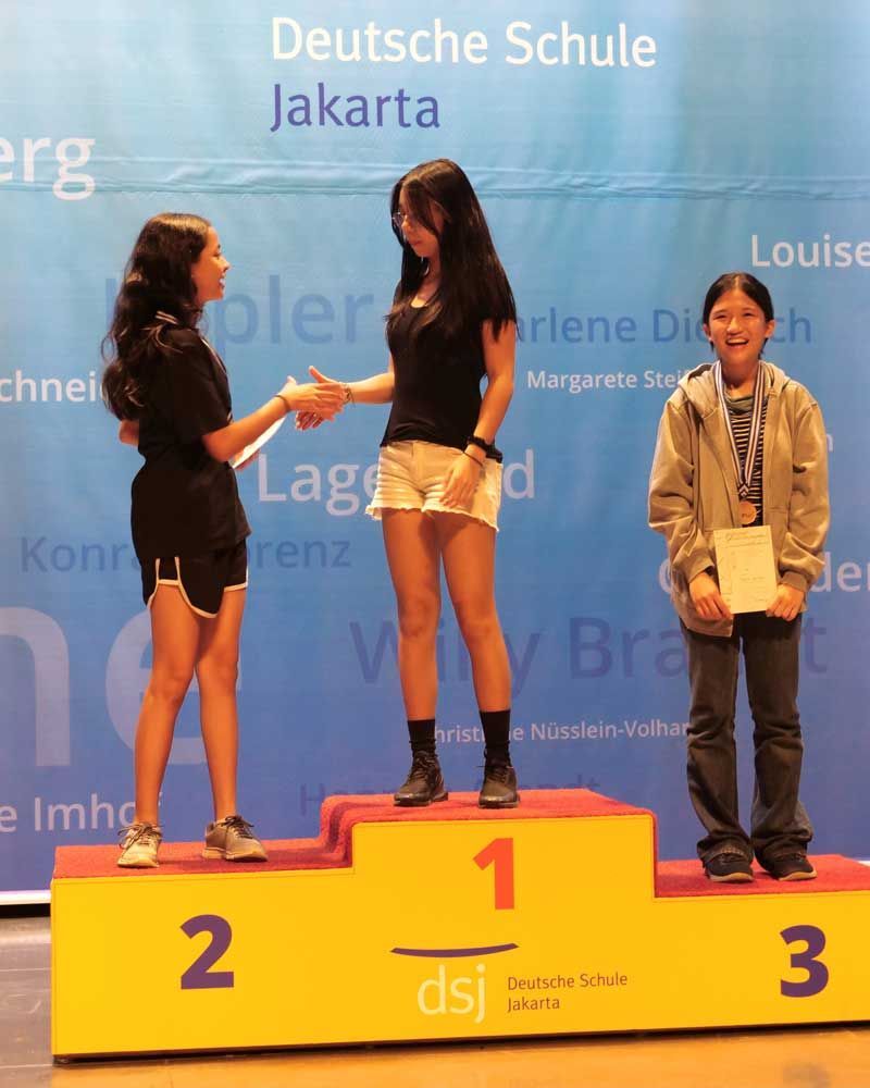 Three girls standing on a podium with the number 1 on it