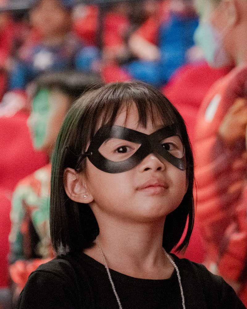 A little girl wearing a black mask is looking up.