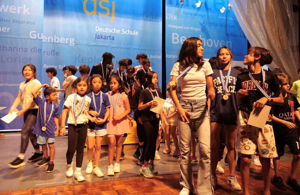A group of children are walking on a stage with medals around their necks.