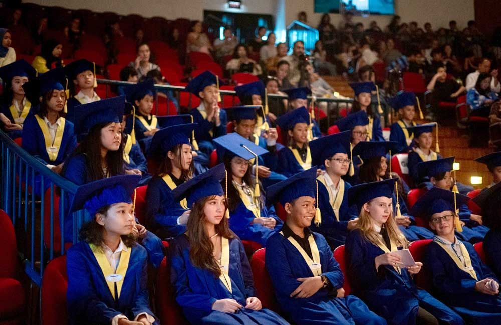 A group of graduates are sitting in a auditorium wearing graduation caps and gowns.