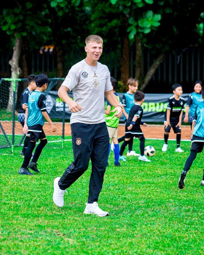 A man is walking on a soccer field with a group of children playing soccer.