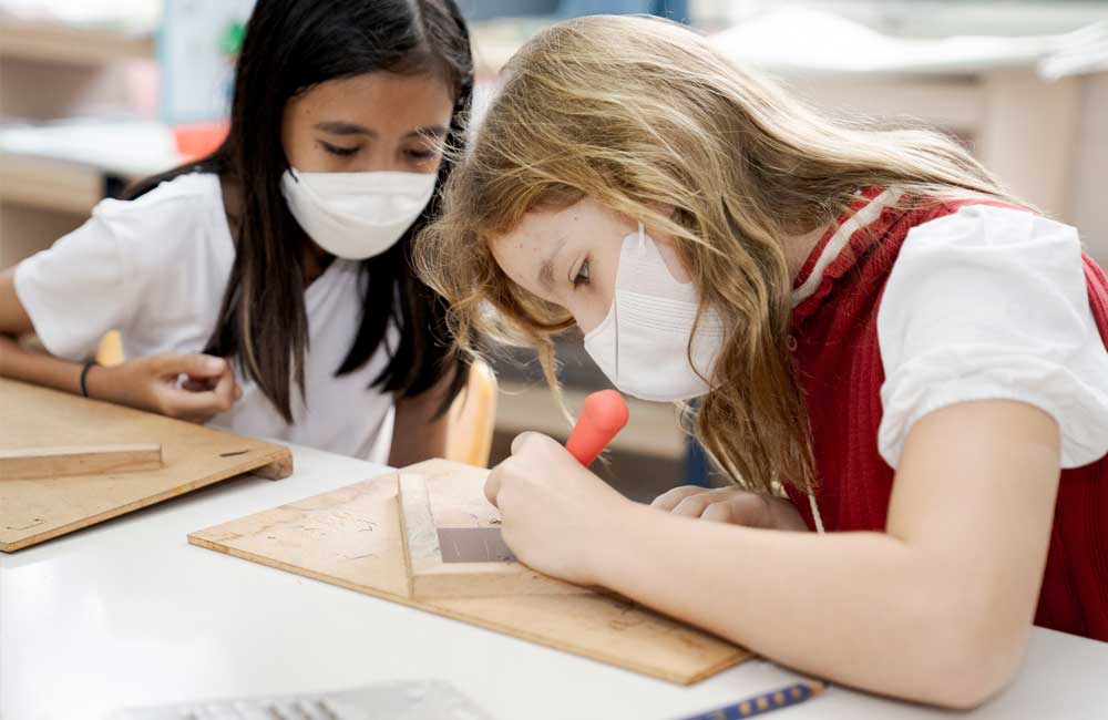 Two girls wearing face masks are sitting at a table in a classroom.