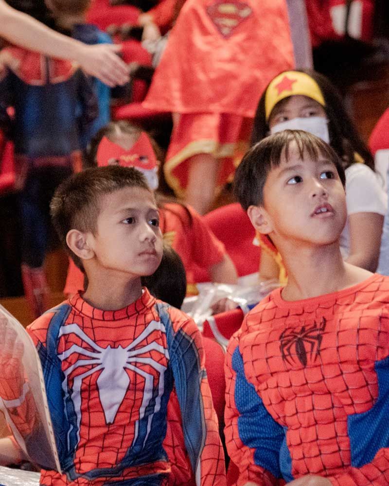 Two boys in spiderman costumes are sitting in a crowd