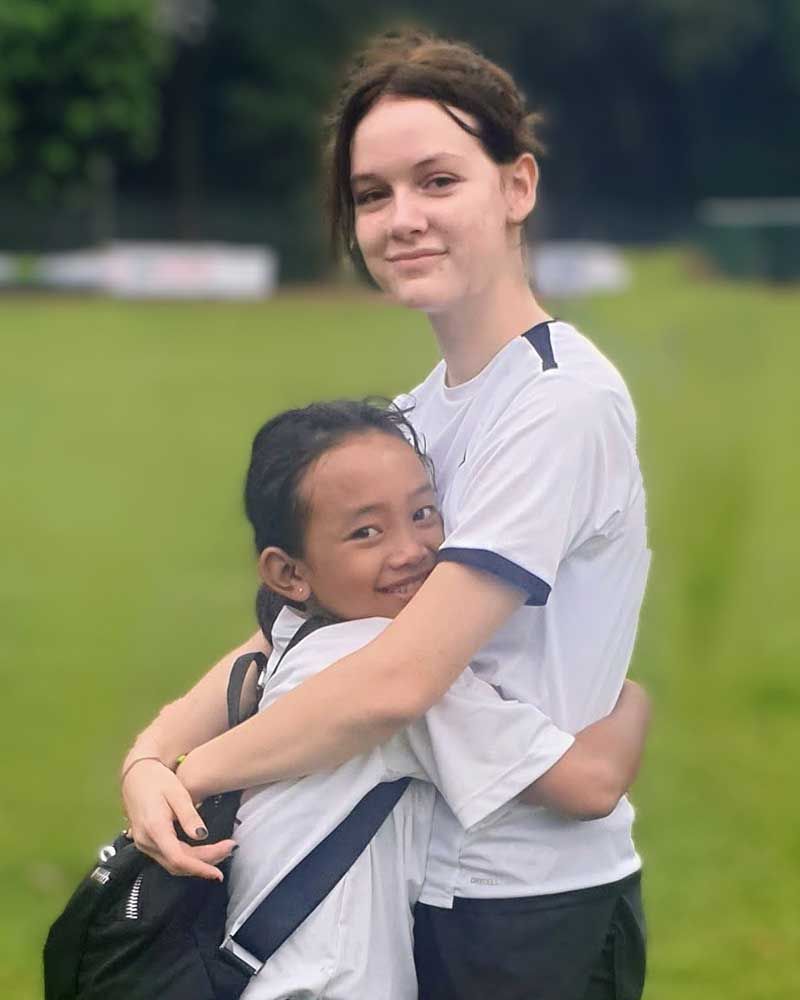 A girl in a white shirt is hugging a little girl in a field.