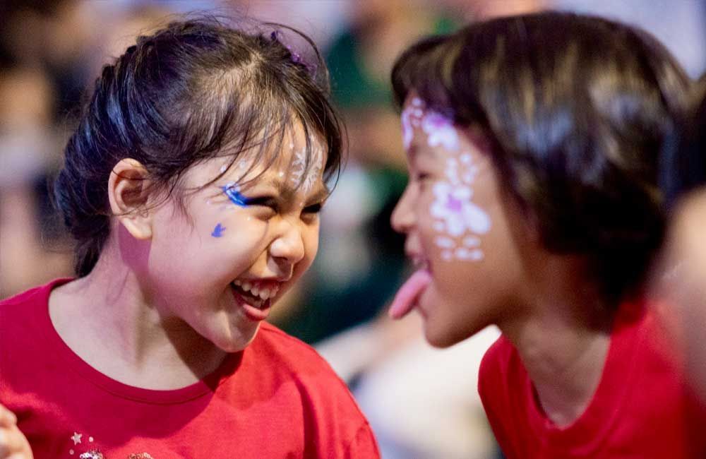 A boy and a girl with face paint on their faces are making funny faces.