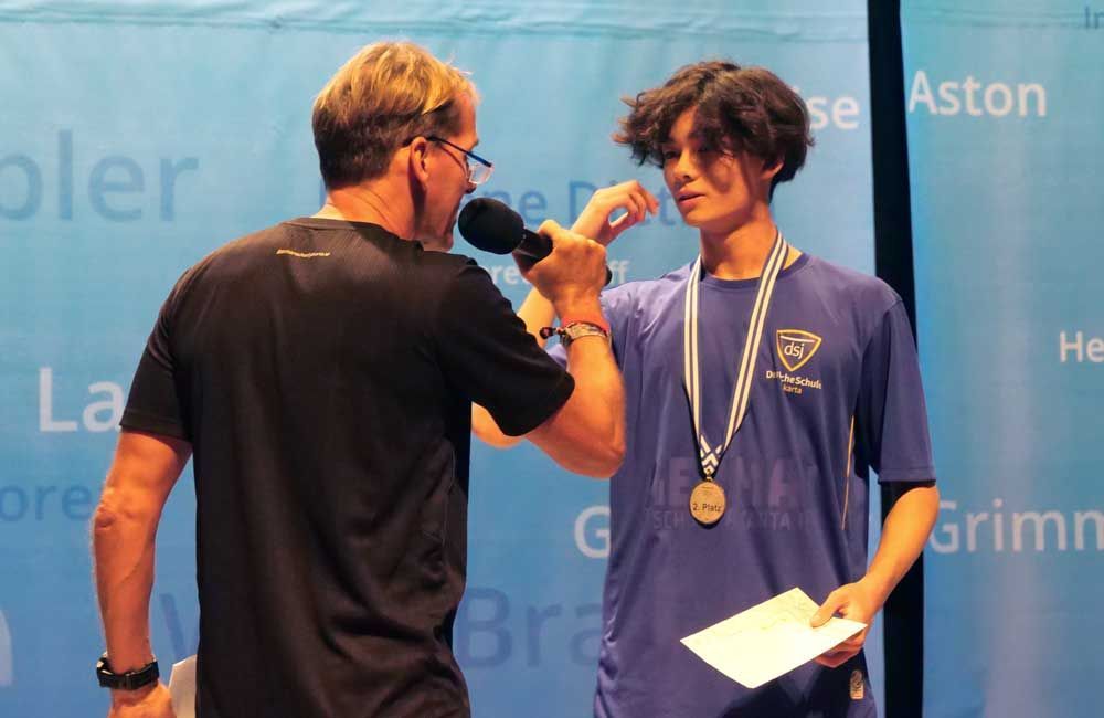 A man is talking into a microphone next to a boy with a medal around his neck