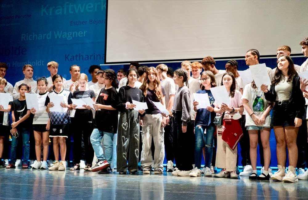 A group of young people are standing on a stage holding papers.