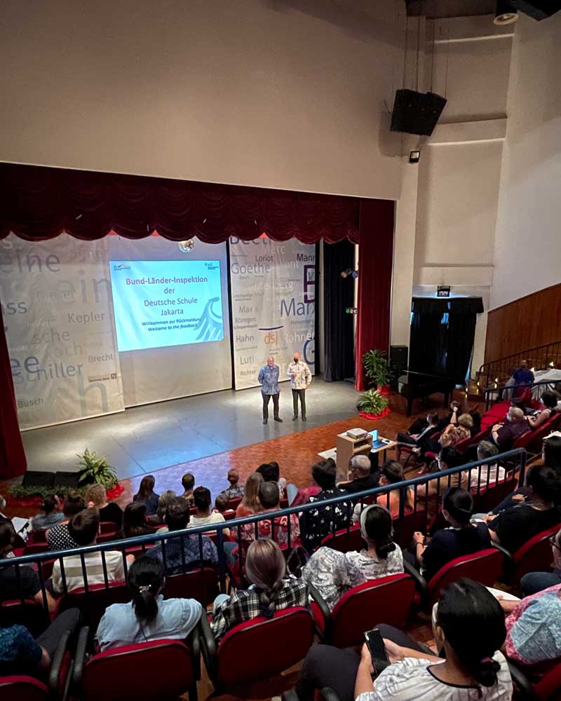 A group of people are sitting in an auditorium watching a presentation on a stage.